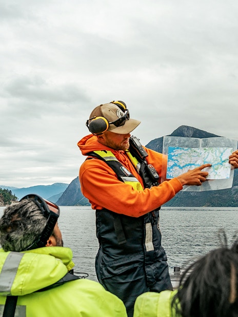 Guide showing map on RIB boat during Tromso whale safari with mountains in background.