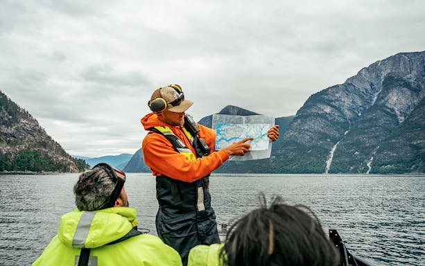 Guide showing map on RIB boat during Tromso whale safari with mountains in background.