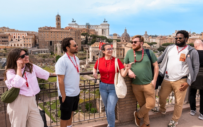 Tour group enjoying view of Roman Forum with Colosseum and Palatine Hill in background.