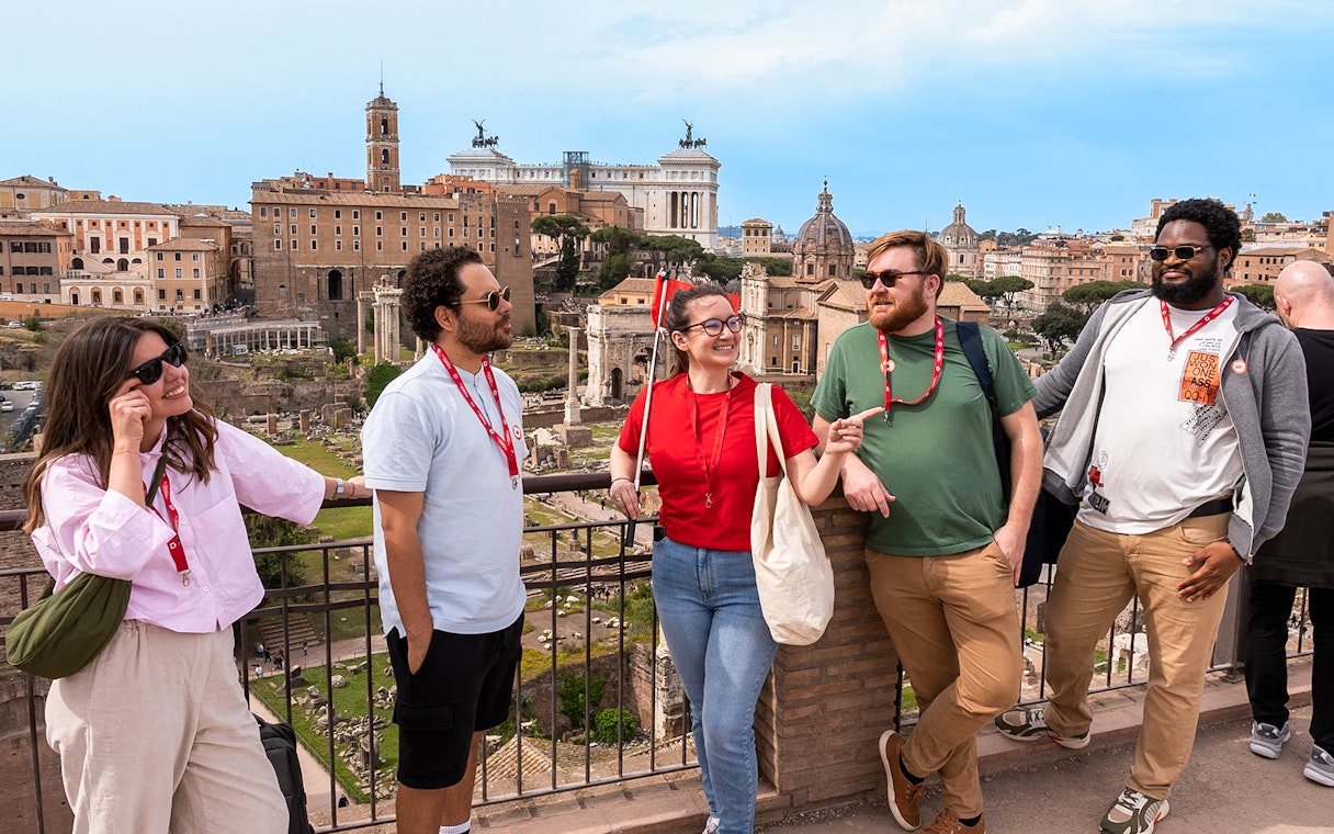 Tour group enjoying view of Roman Forum with Colosseum and Palatine Hill in background.
