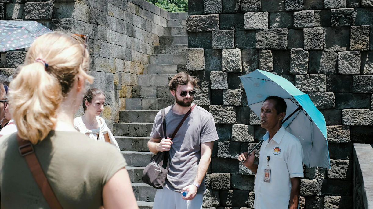 Tour guide with umbrella explaining Borobudur Temple to visitors.