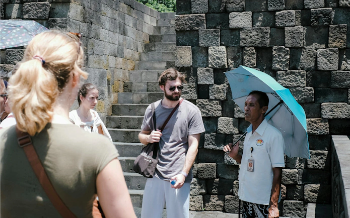 Tour guide with umbrella explaining Borobudur Temple to visitors.