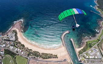 Skydiver descending over Shellharbour beach, Sydney, with ocean and coastline view.