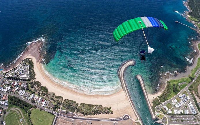 Skydiver descending over Shellharbour beach, Sydney, with ocean and coastline view.