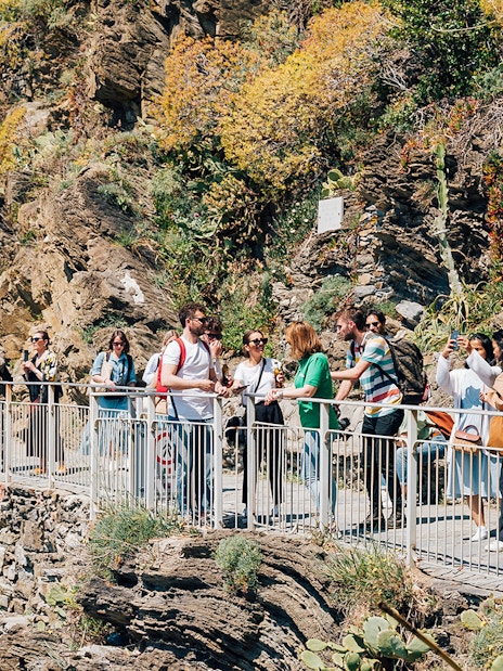 Tourists walking along a scenic cliffside path in Cinque Terre, Italy.
