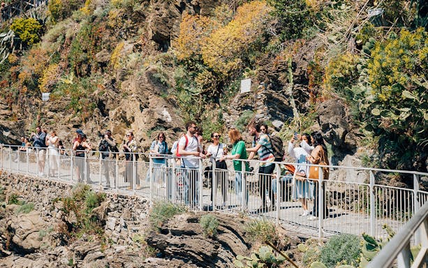 Tourists walking along a scenic cliffside path in Cinque Terre, Italy.