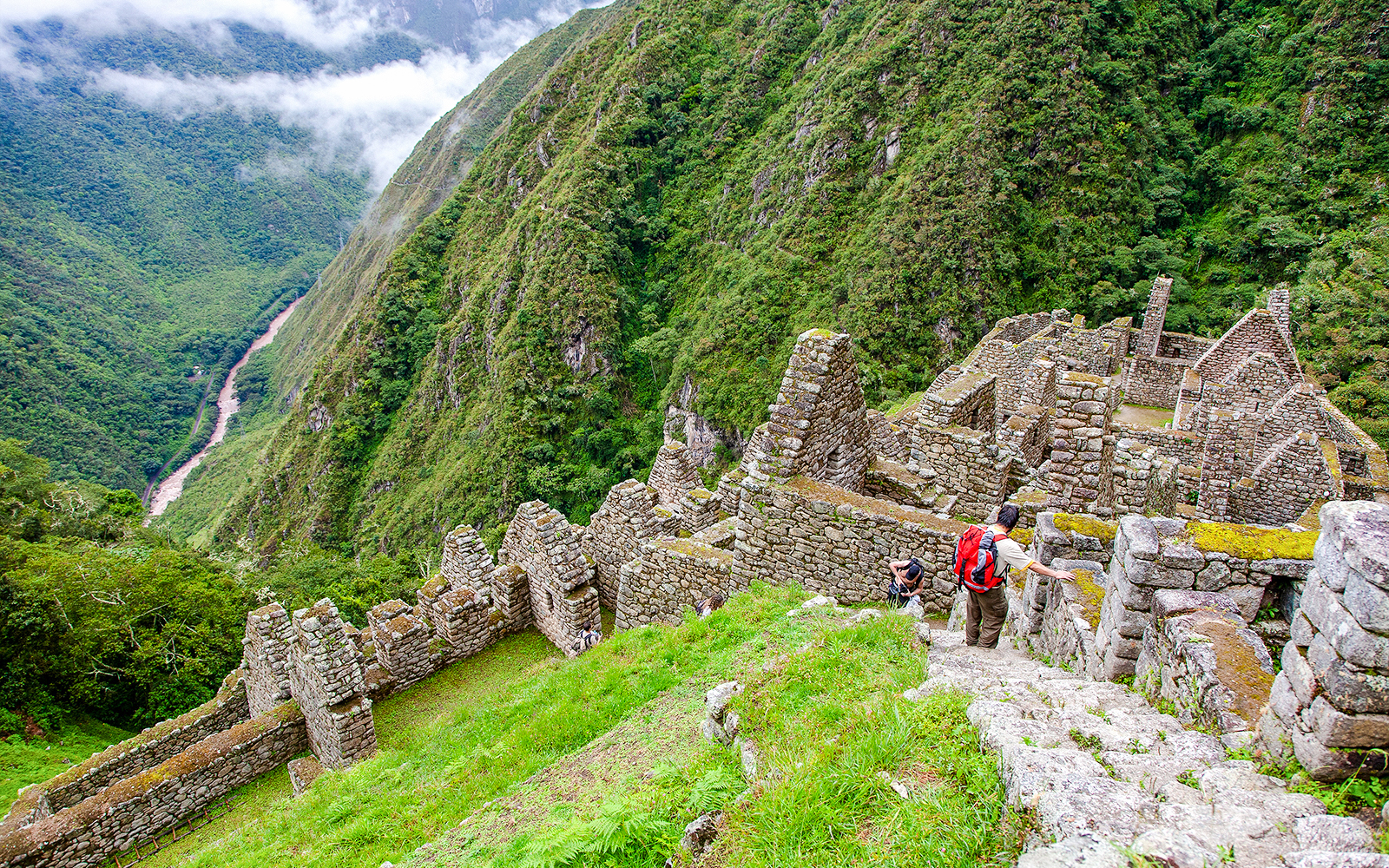 Wiñay Wayna ruins with hikers descending stone steps, surrounded by lush green mountains in Peru.