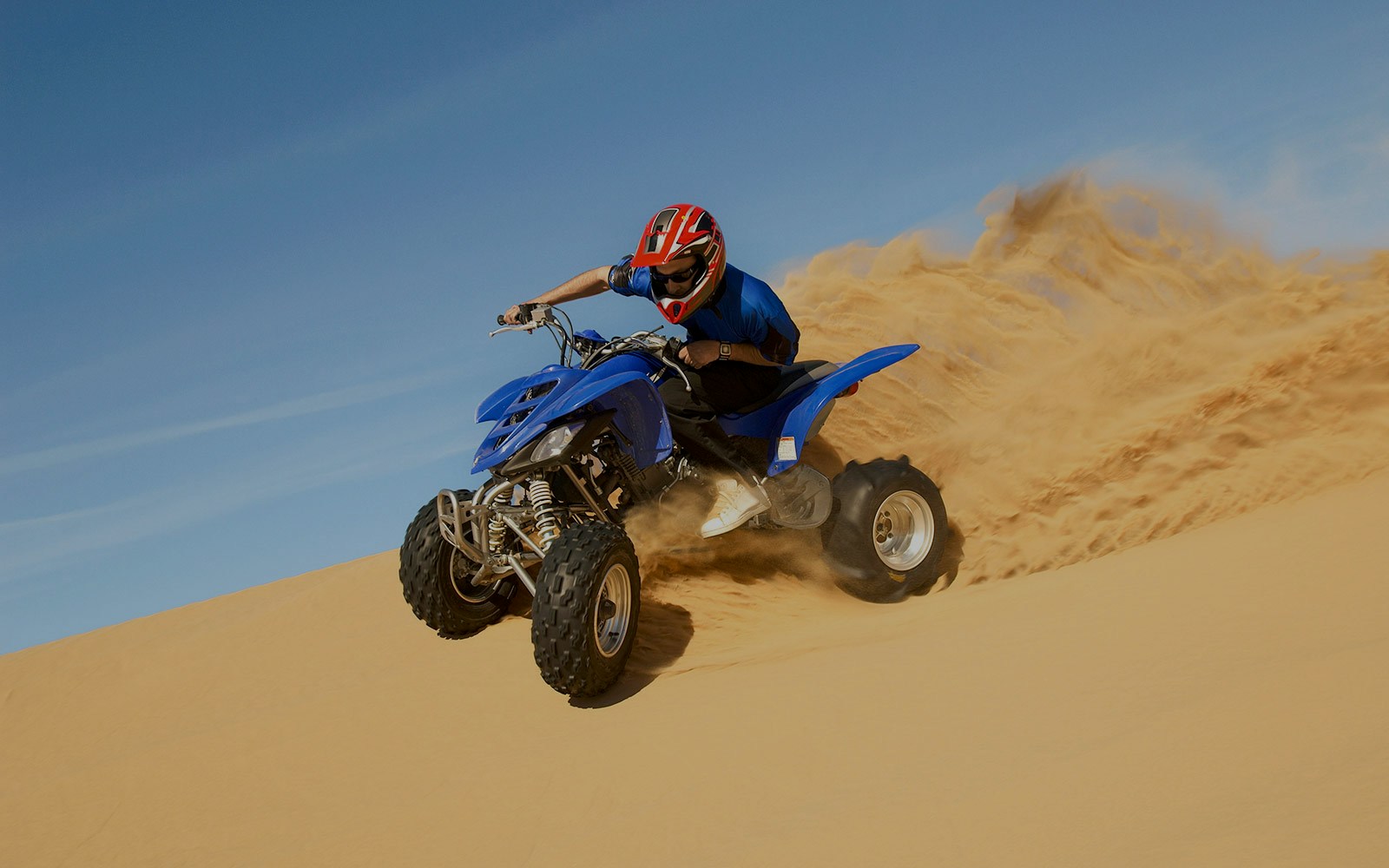 Man riding a blue quad bike on a sandy desert dune.