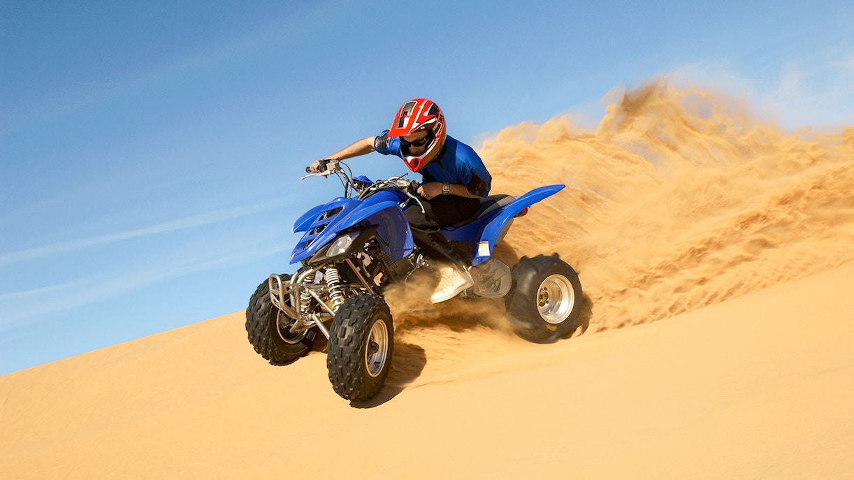 Man riding a blue quad bike on a sandy desert dune.
