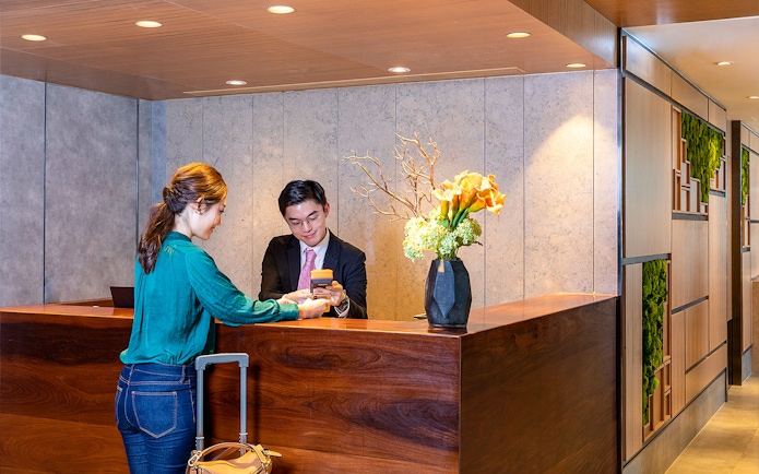 Receptionist assisting traveler at Plaza Premium Lounge check-in counter.