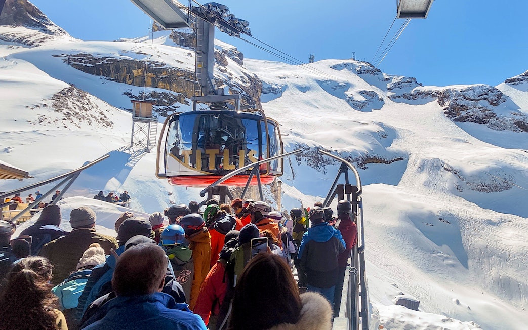 Mount Titlis Rotair cable car with tourists boarding, surrounded by snowy Swiss Alps.