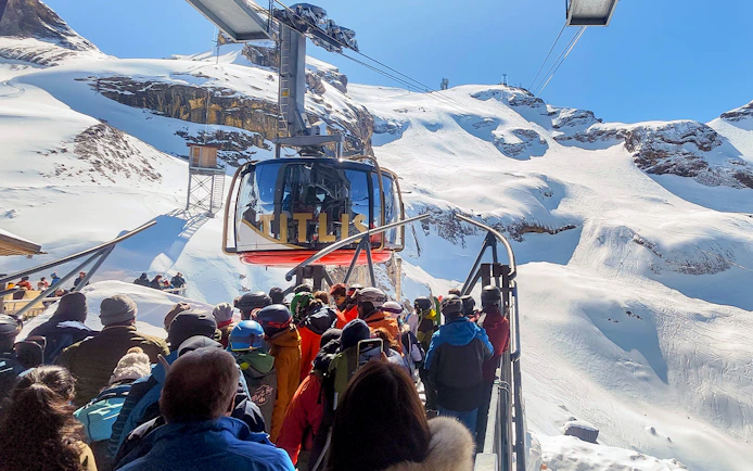 Mount Titlis Rotair cable car with tourists boarding, surrounded by snowy Swiss Alps.