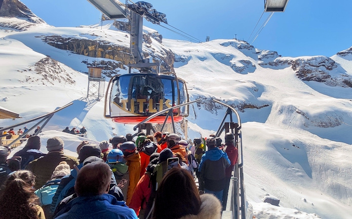 Mount Titlis Rotair cable car with tourists boarding, surrounded by snowy Swiss Alps.