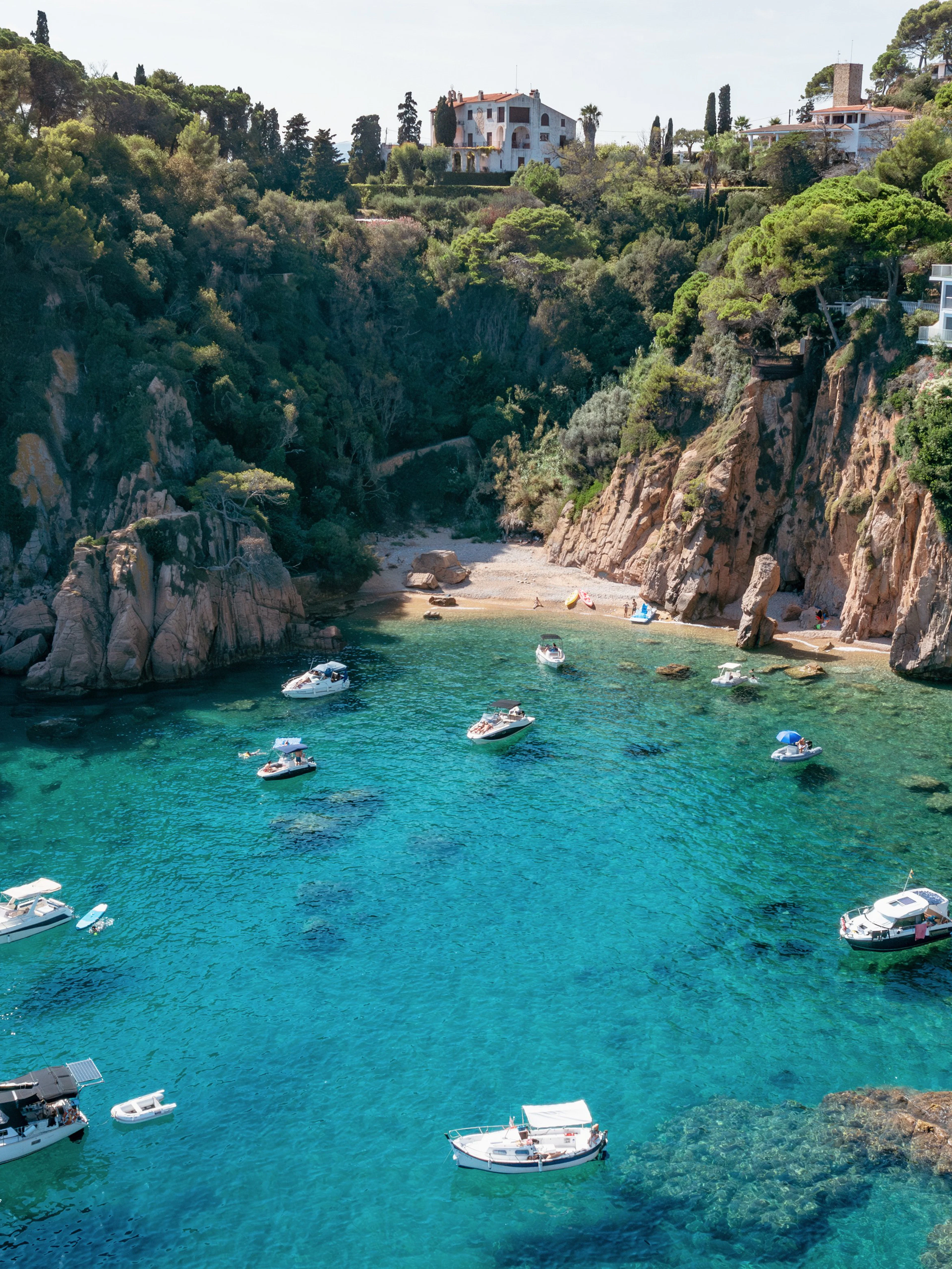Blanes bay with turquoise water, rocky cliffs, and white villas on a green hillside.