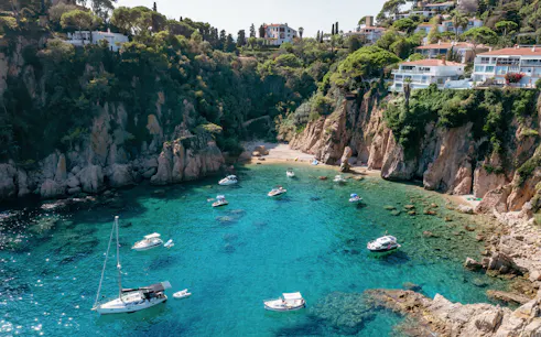 Blanes bay with turquoise water, rocky cliffs, and white villas on a green hillside.