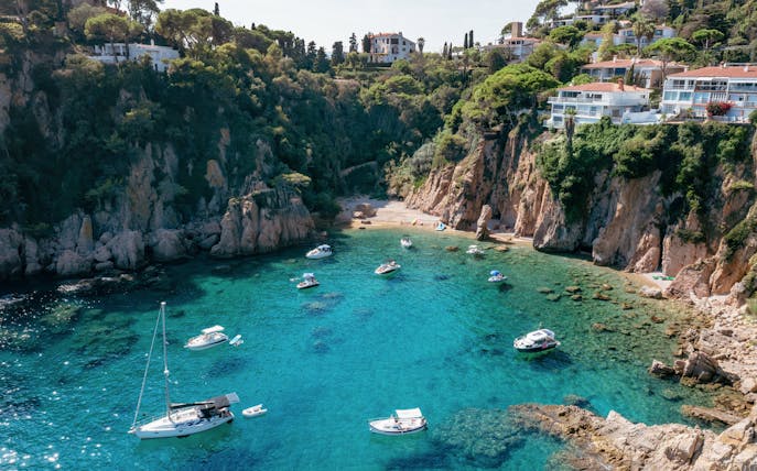 Blanes bay with turquoise water, rocky cliffs, and white villas on a green hillside.