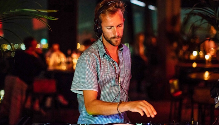 DJ performing at ADAM Lookout in Amsterdam with city skyline in the background.