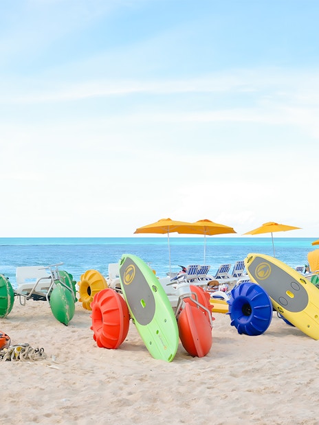 Colorful kayaks and water bikes on a sandy beach in Bimini, Bahamas.