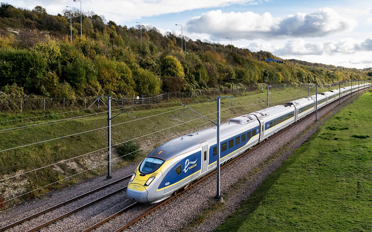 Eurostar train traveling through countryside with green hills and cloudy sky.