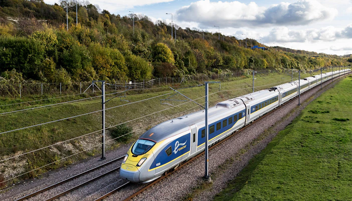 Eurostar train traveling through countryside with green hills and cloudy sky.