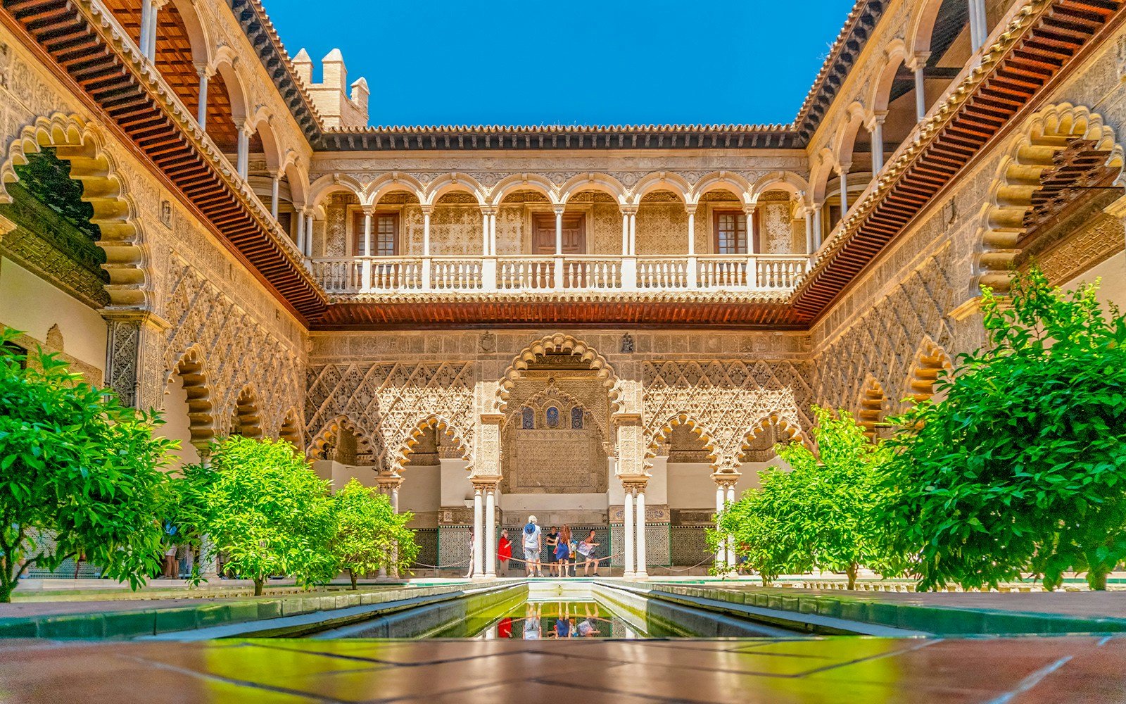 Alcazar of Seville courtyard with intricate arches and reflecting pool.