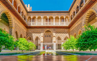 Alcazar of Seville courtyard with intricate arches and lush greenery.
