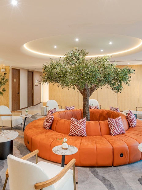 Coral Airport Lounge seating area with tree centerpiece at Suvarnabhumi Airport.