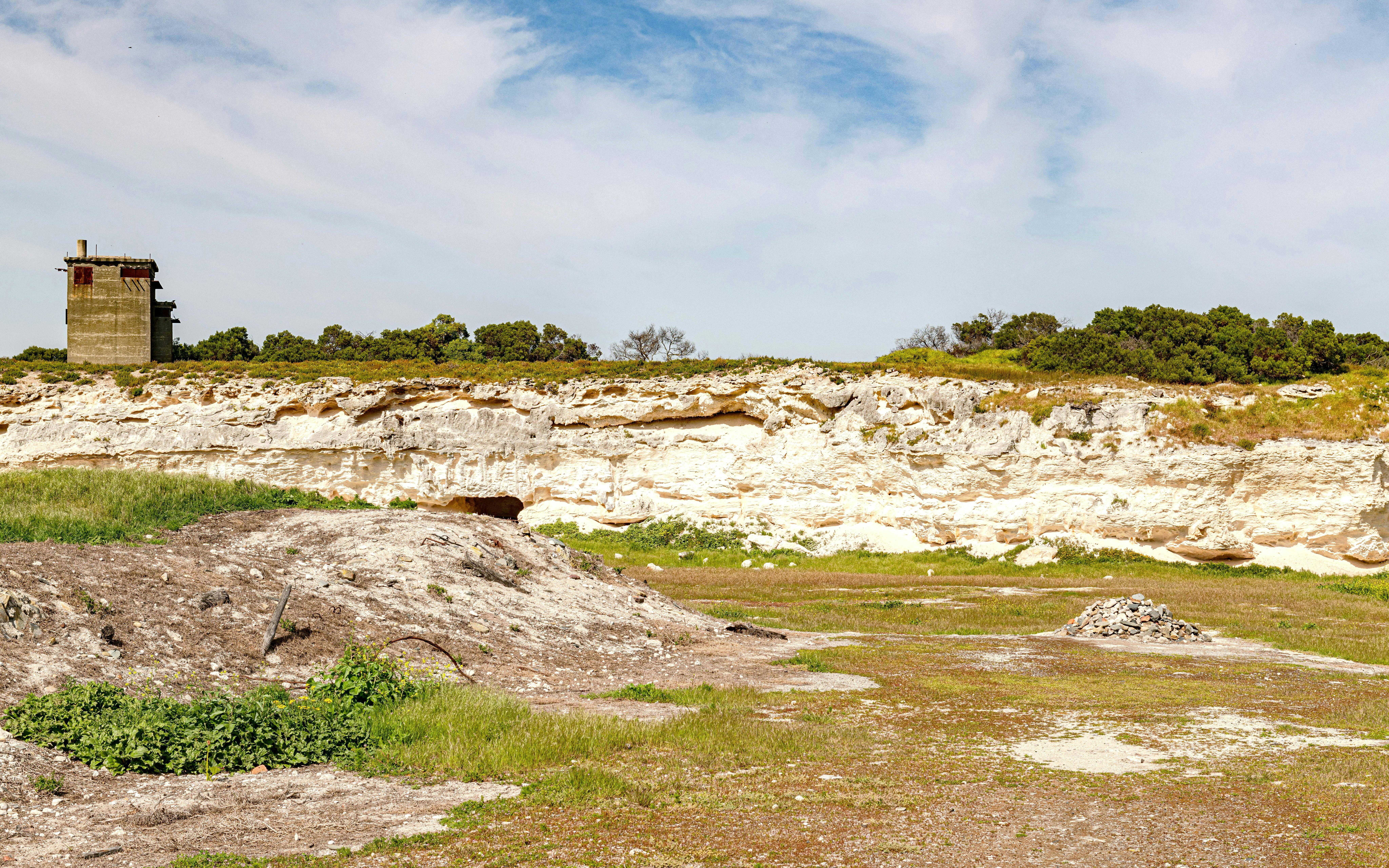 Quarry at Robben Island Prison with stone pile and greenery, Cape Town, South Africa.