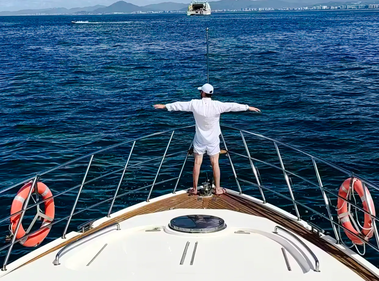 Person standing on yacht deck with arms outstretched, Sanya Phoenix Island tour.