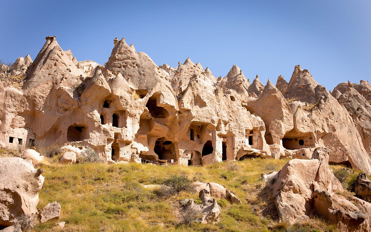 Ancient rock formations and cave dwellings in Cappadocia, Turkey, under a clear blue sky.