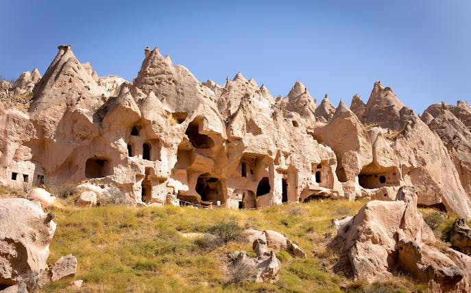 Ancient rock formations and cave dwellings in Cappadocia, Turkey, under a clear blue sky.