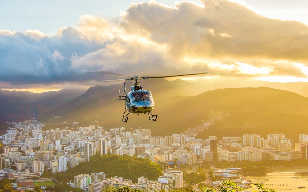 Helicopter taking off from Urca mountain helipad at sunset, overlooking Rio de Janeiro, Brazil.