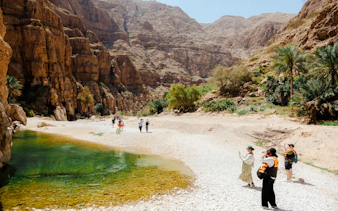 Hikers exploring Wadi Shab's rocky landscape and emerald pools, Oman.