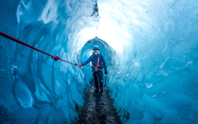 Guests hiking inside Blue Ice Cave in Vatnajökull, Iceland, holding a safety rope.
