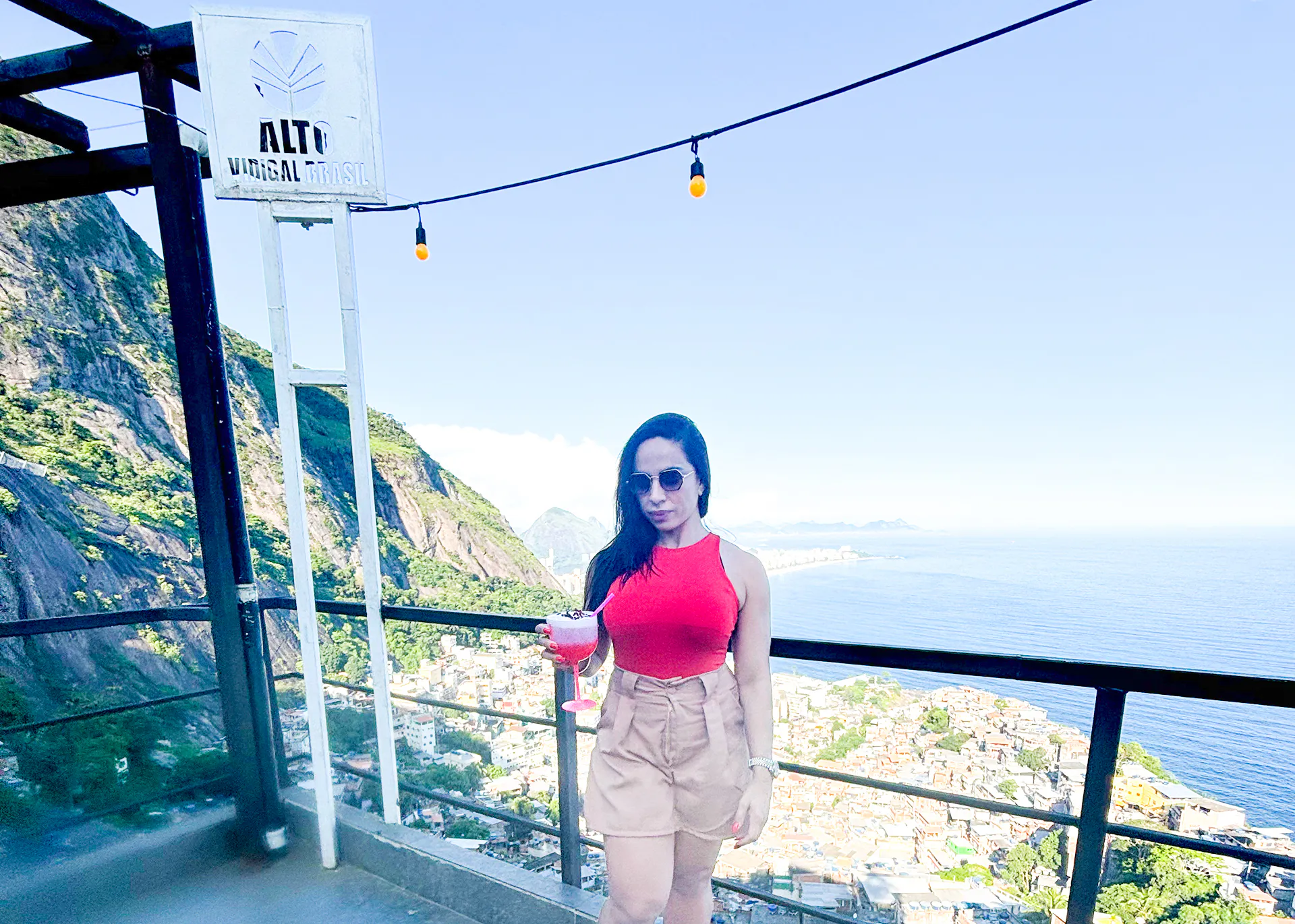 Woman enjoying a drink with panoramic view of Vidigal and ocean, Rio de Janeiro.