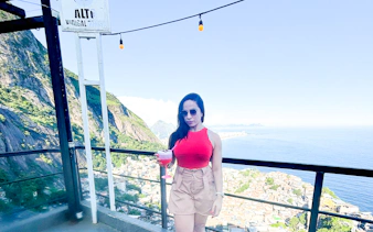 Woman enjoying a drink with panoramic view of Vidigal and ocean, Rio de Janeiro.