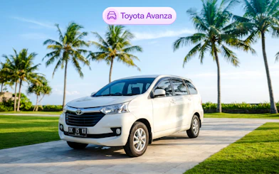 Toyota Avanza parked on a sunny day in Bali with palm trees in the background.