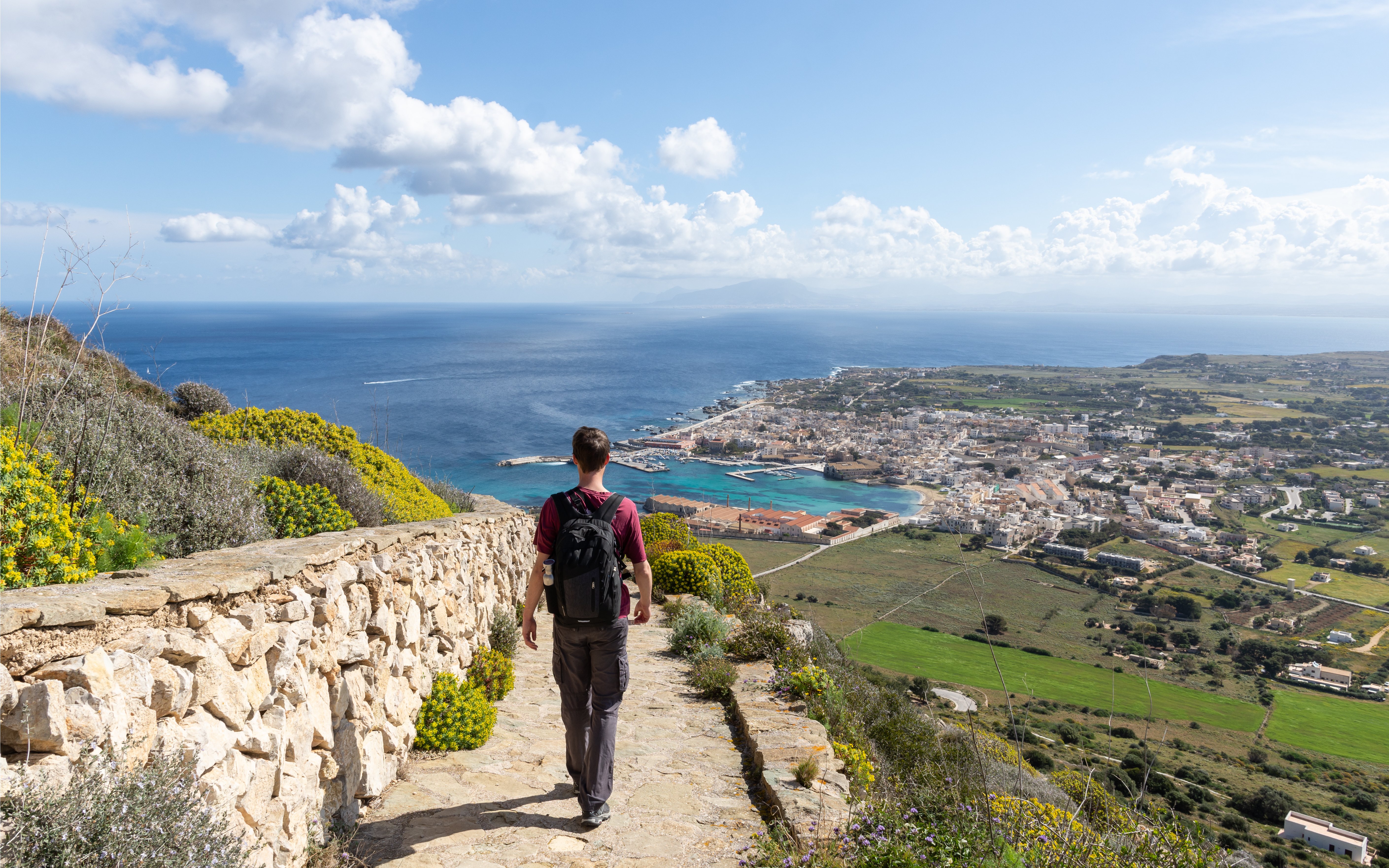 Man walking along a stone path overlooking Favignana village and coastline, Sicily.