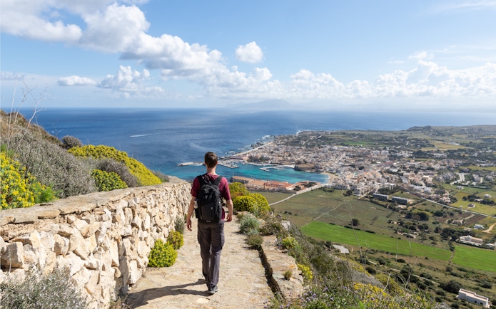 Man walking along a stone path overlooking Favignana village and coastline, Sicily.
