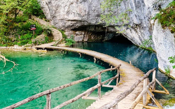 Curved wooden bridge over turquoise lake at Plitvice Lakes National Park.