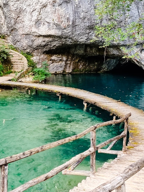 Curved wooden bridge over turquoise lake at Plitvice Lakes National Park.