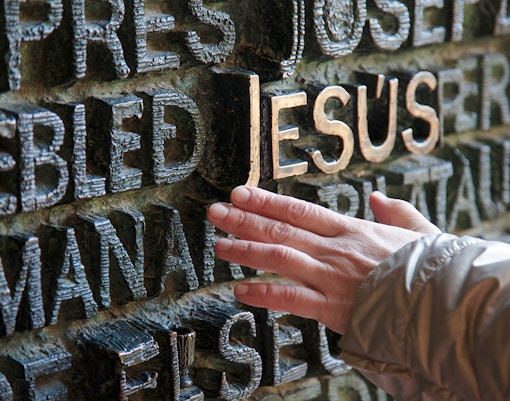 Hand touching ornate bronze doors with raised text at Sagrada Familia, Barcelona.