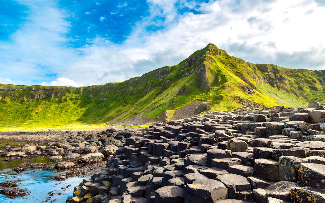 Giant’s Causeway basalt columns with green cliffs in the background, Northern Ireland.