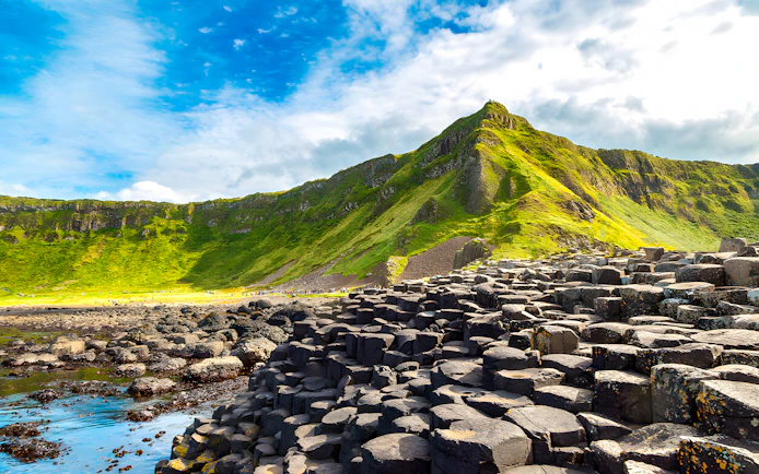 Giant’s Causeway basalt columns with green cliffs in the background, Northern Ireland.