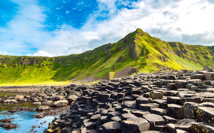 Giant’s Causeway basalt columns with green cliffs in the background, Northern Ireland.