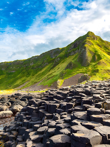 Giant’s Causeway basalt columns with green cliffs in the background, Northern Ireland.