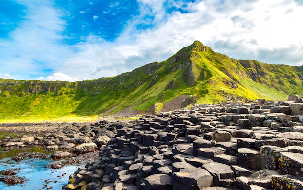 Giant’s Causeway basalt columns with green cliffs in the background, Northern Ireland.