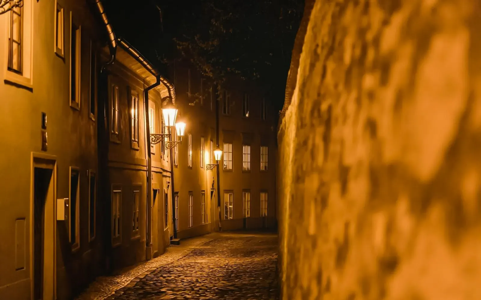 Narrow cobblestone street near Prague Castle illuminated by street lamps at night.
