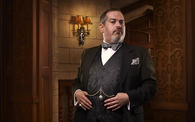 Man in formal attire standing in a vintage theater setting for The Mousetrap.