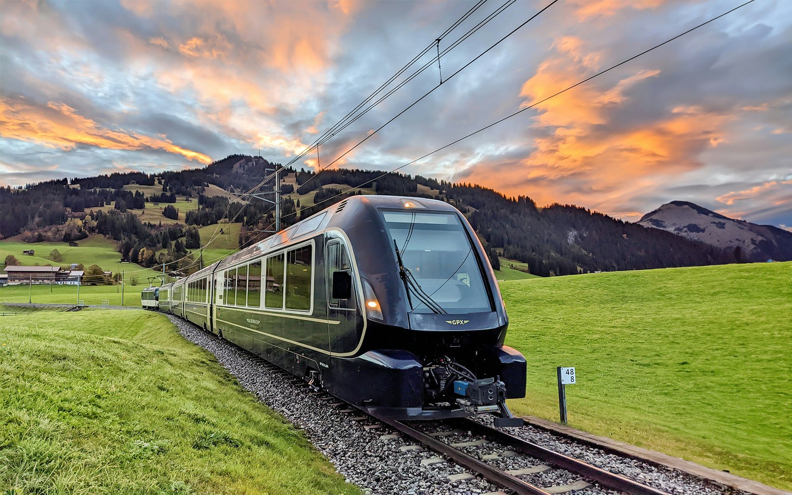 GoldenPass Express train traveling through scenic Swiss countryside near Interlaken at sunset.